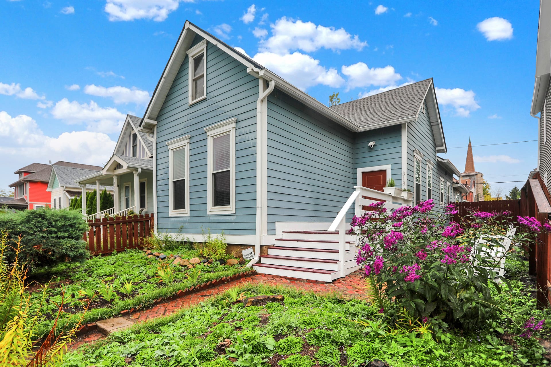 The Sanders, a restored 1900 blue cottage in Bates-Hendricks, Indianapolis, with brick garden path and steep gabled roof